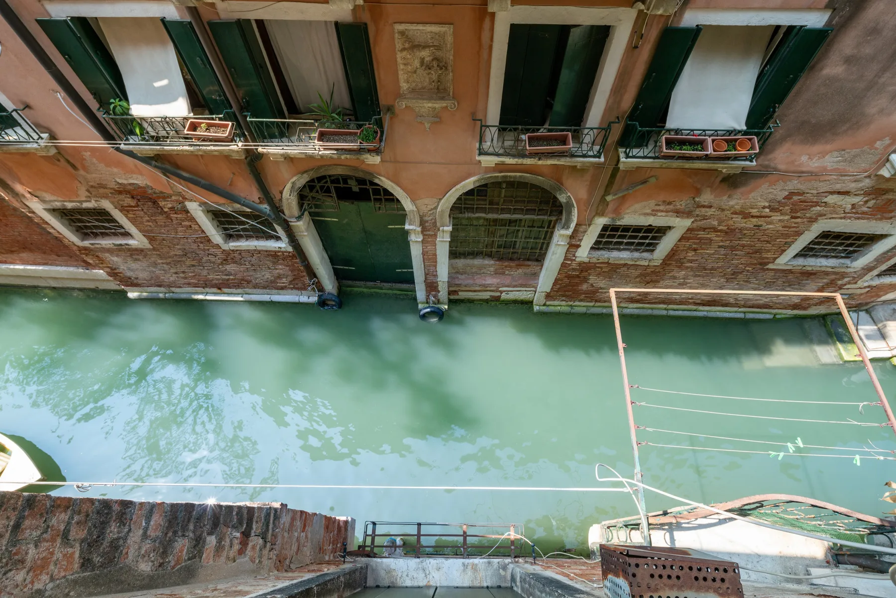 Un canal bordea un edificio antiguo con aberturas arqueadas y jardineras en las ventanas.