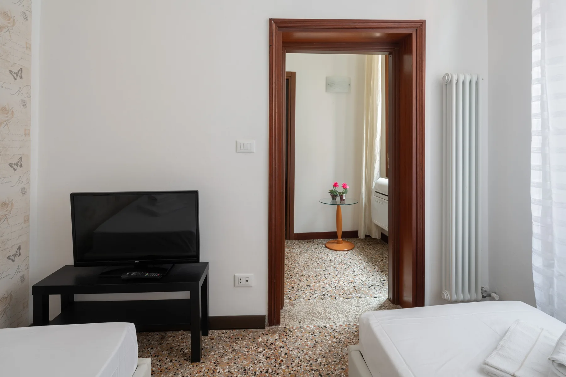 Un dormitorio luminoso con un televisor, dos camas y una puerta que da a otra habitación.