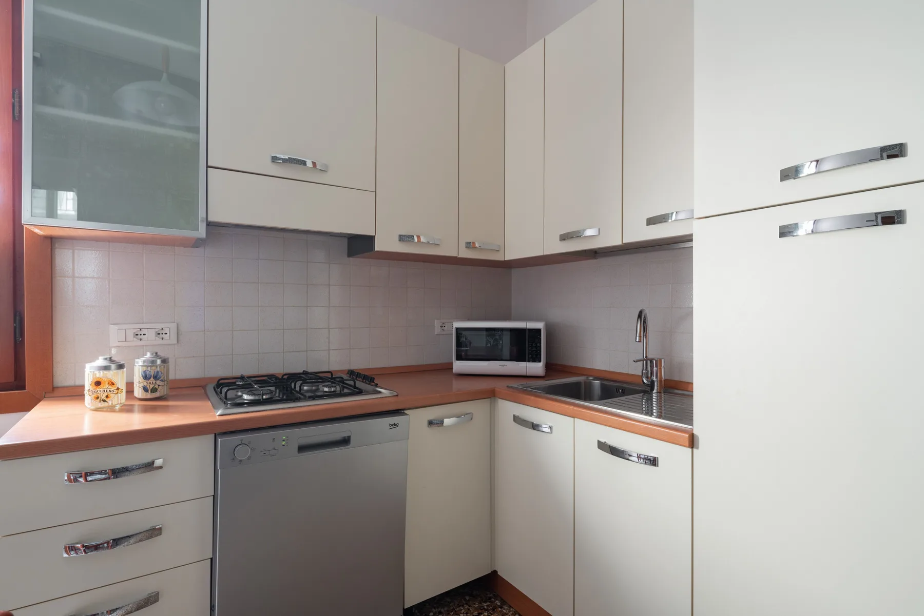 Una cocina compacta con gabinetes claros, una estufa, un microondas y un fregadero.