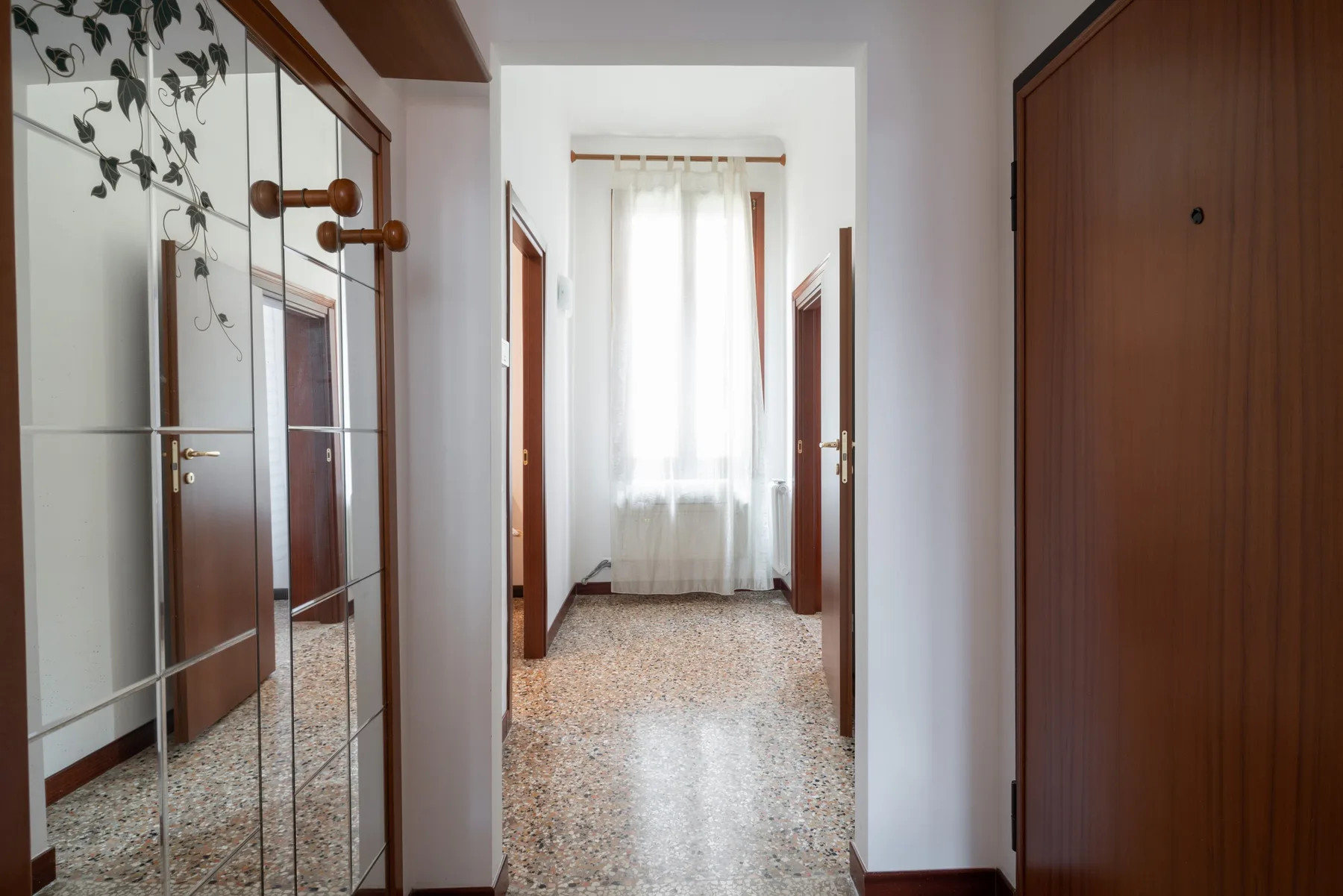 Un pasillo luminoso con puertas de armario con espejo y una ventana al fondo.
