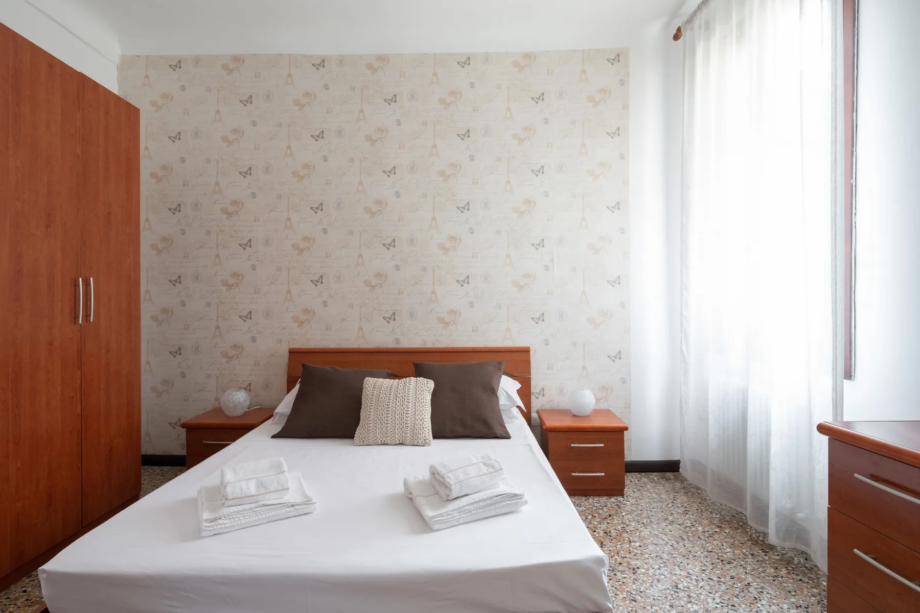 Un dormitorio con una cama bien tendida y papel tapiz estampado.