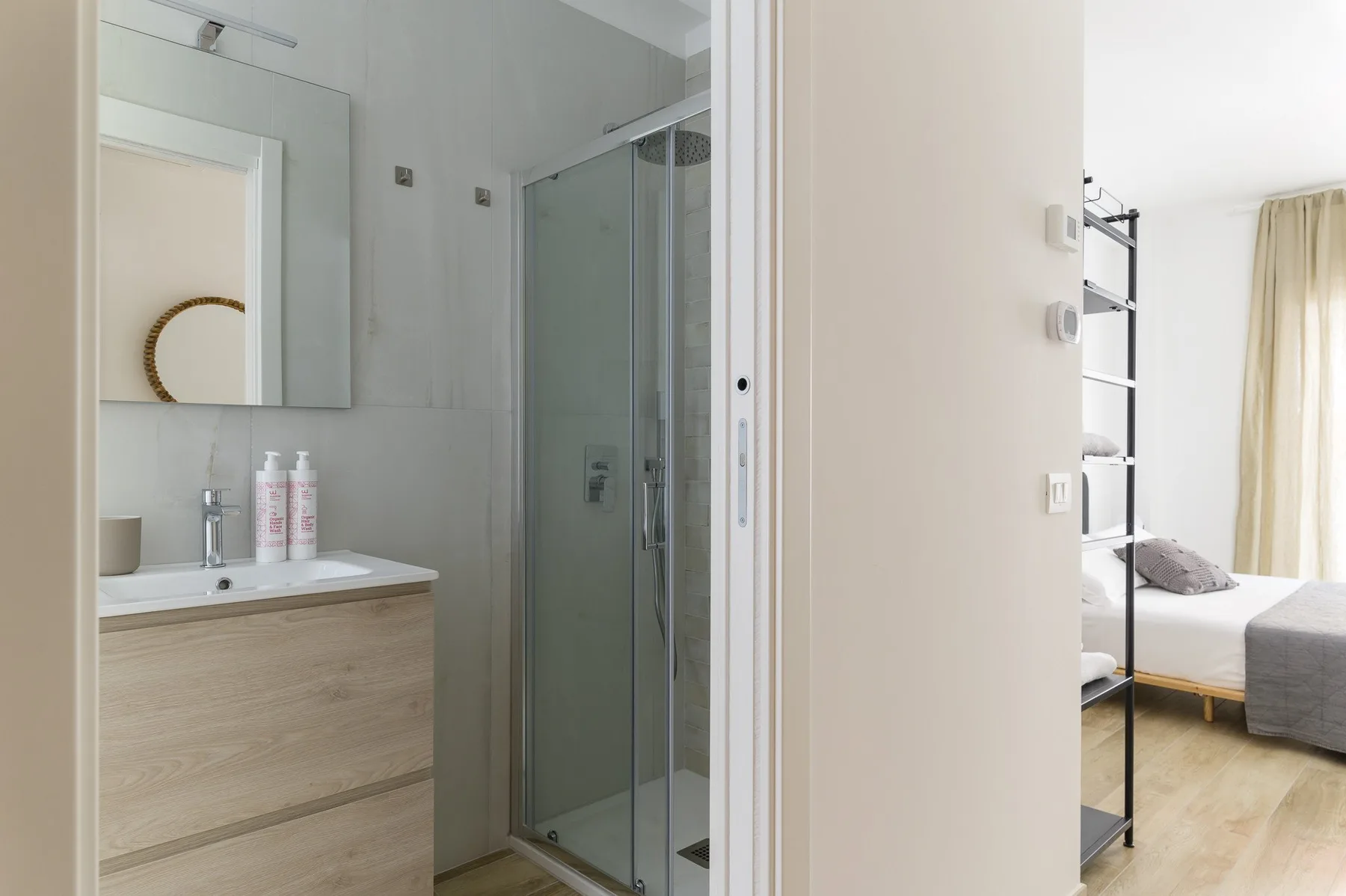 Un baño con lavabo y ducha de vidrio junto a un dormitorio.
