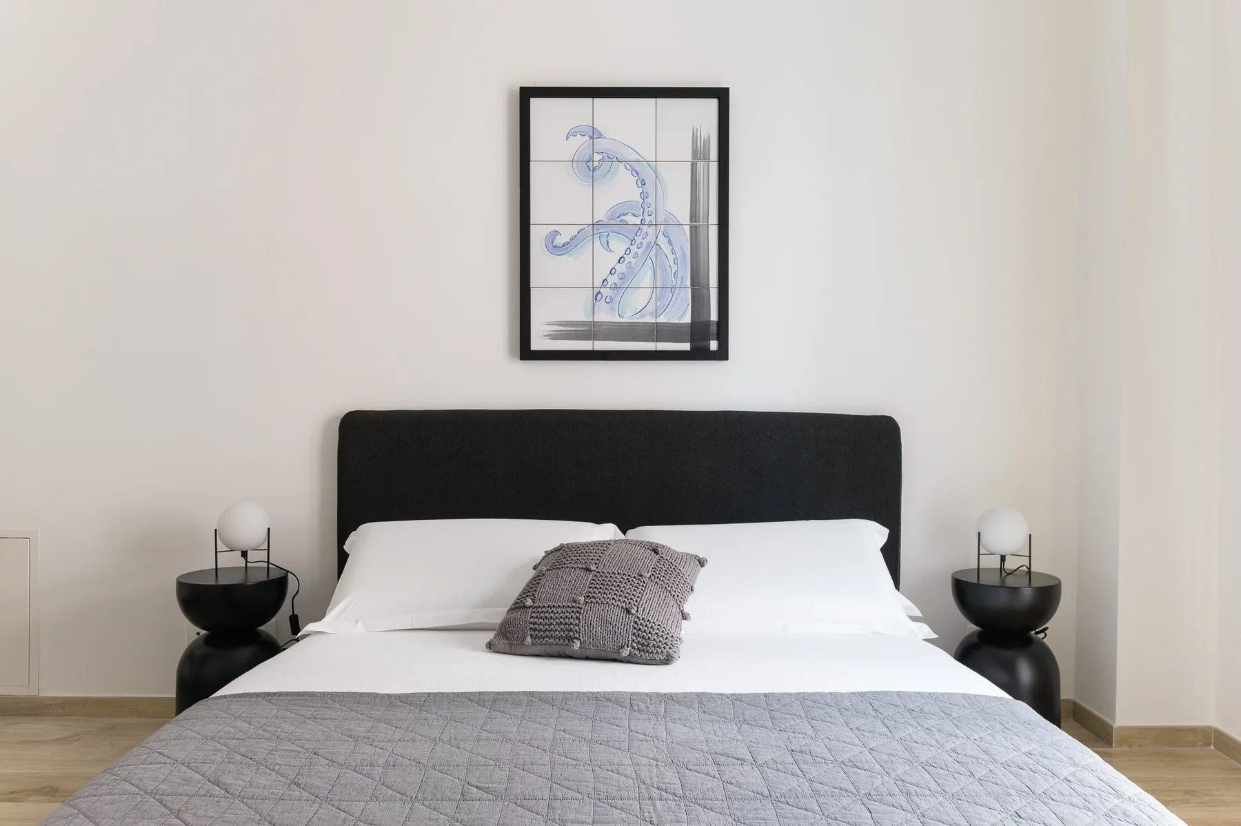 Un dormitorio con una cama bien tendida y un cuadro sobre el cabecero.
