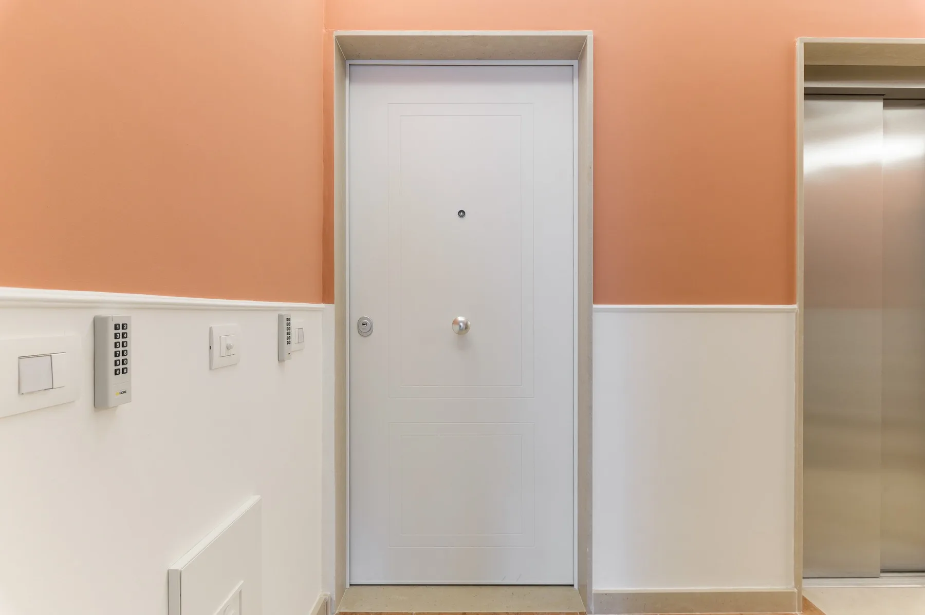 Un pasillo interior con una puerta gris y un ascensor.