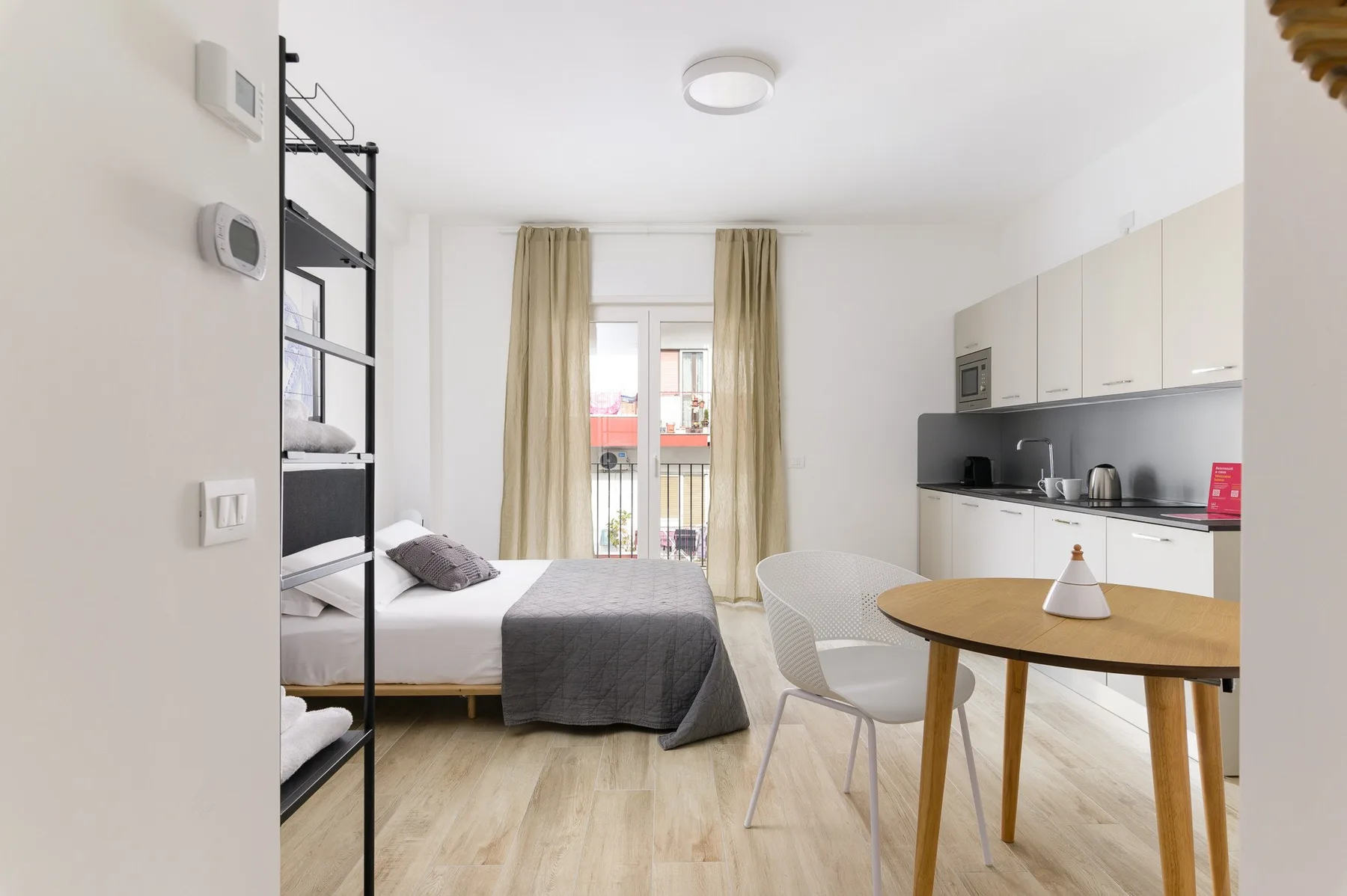 Un estudio luminoso con cama, cocina pequeña y mesa de comedor.