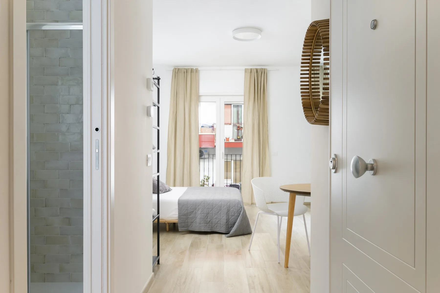 Un dormitorio luminoso con una cama, una mesa pequeña y una ventana con cortinas.