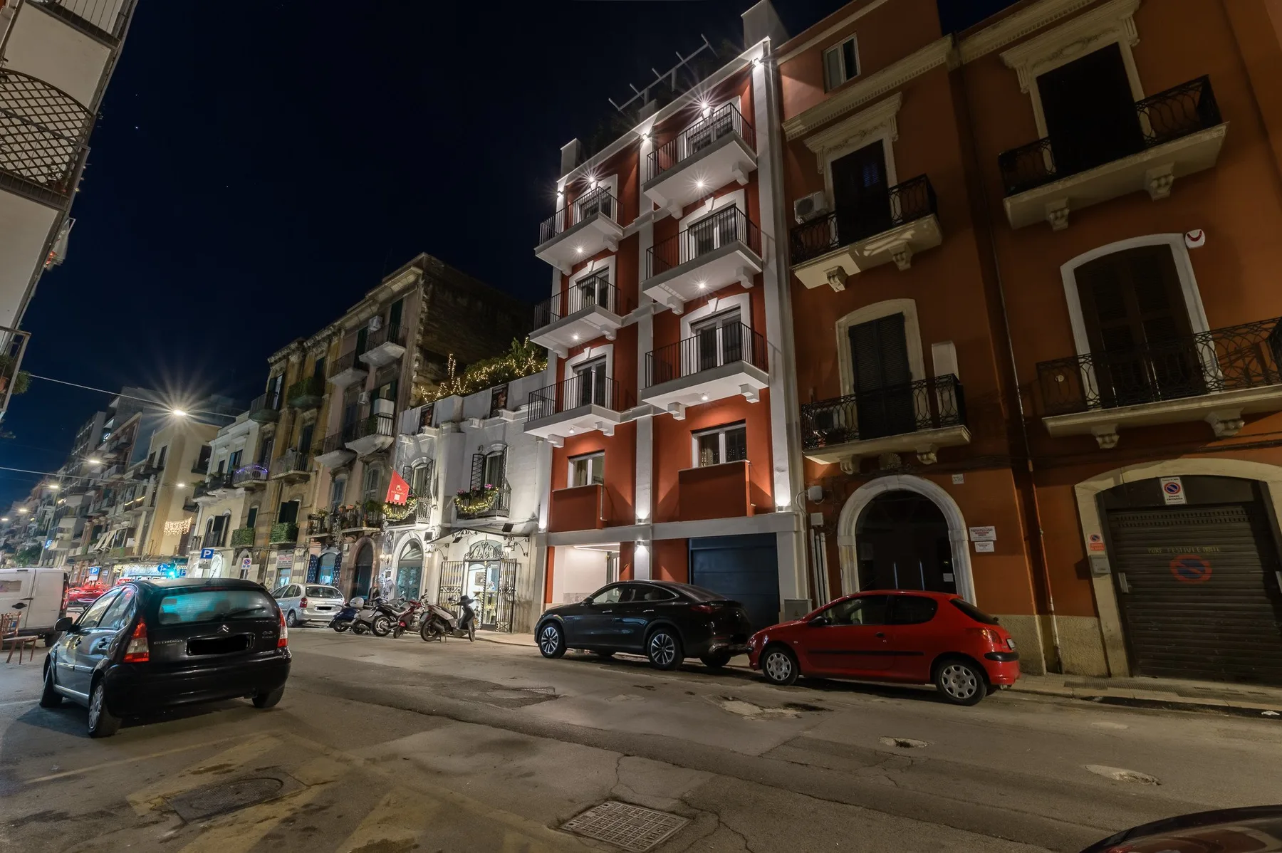 Una calle de noche con edificios iluminados y autos estacionados.