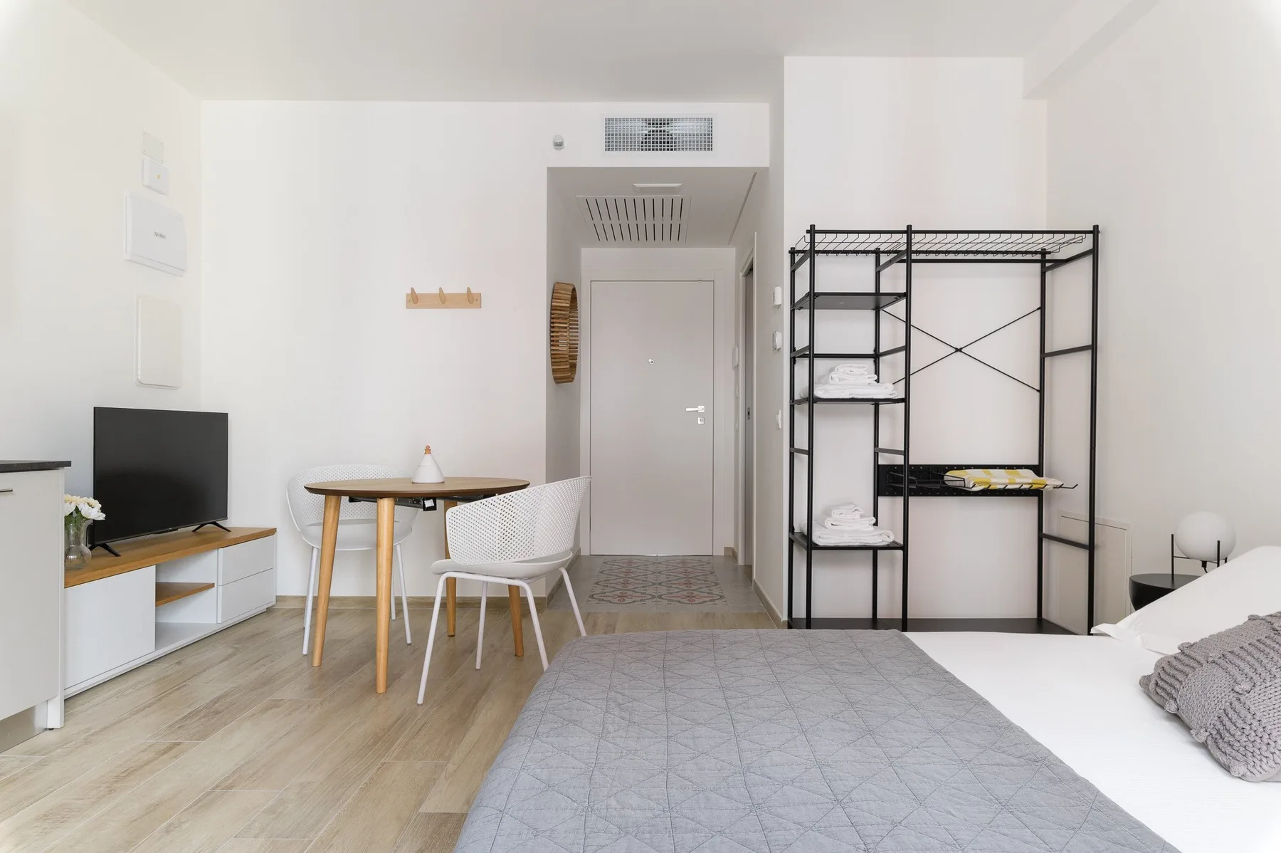 Un dormitorio luminoso con una cama, una mesa pequeña y estanterías abiertas.