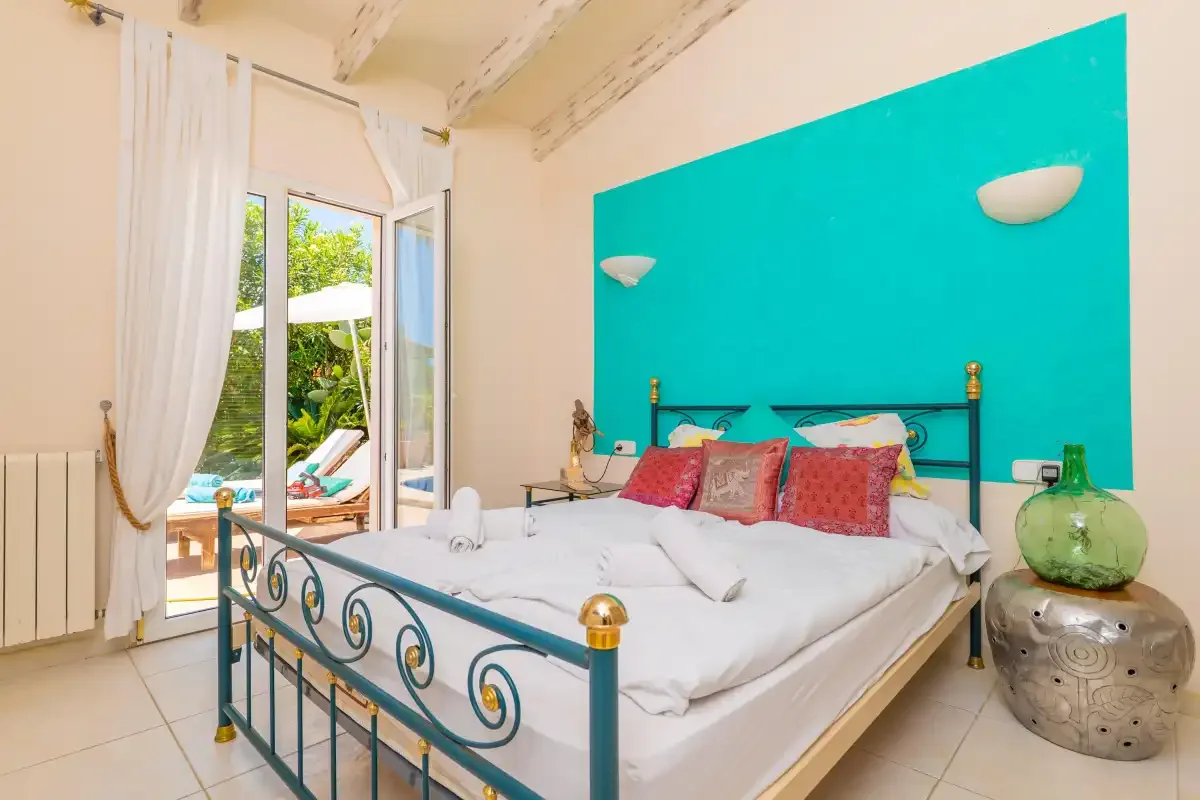 A bedroom with a metal bed, colorful pillows, and a bright turquoise wall.