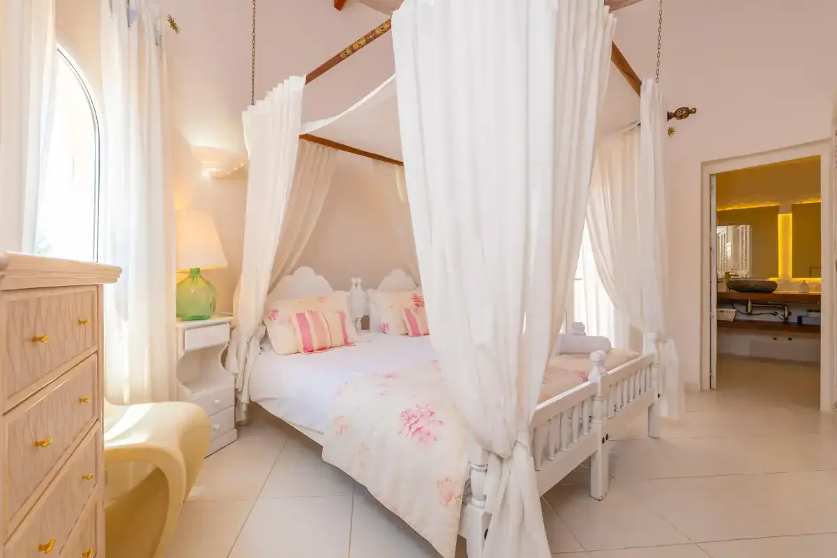 A bright bedroom with a curtained bed and an adjoining bathroom.