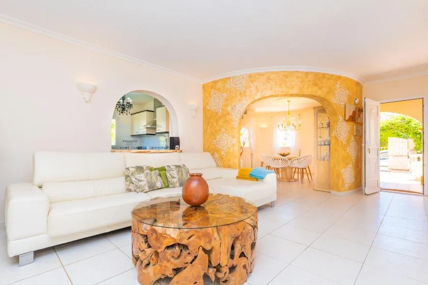 A bright living room with white seating and an arched opening to a dining area.