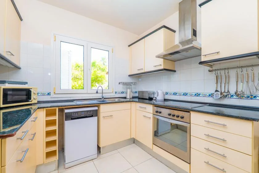 A bright kitchen with pale cabinets, dark countertops, and a window above the sink.