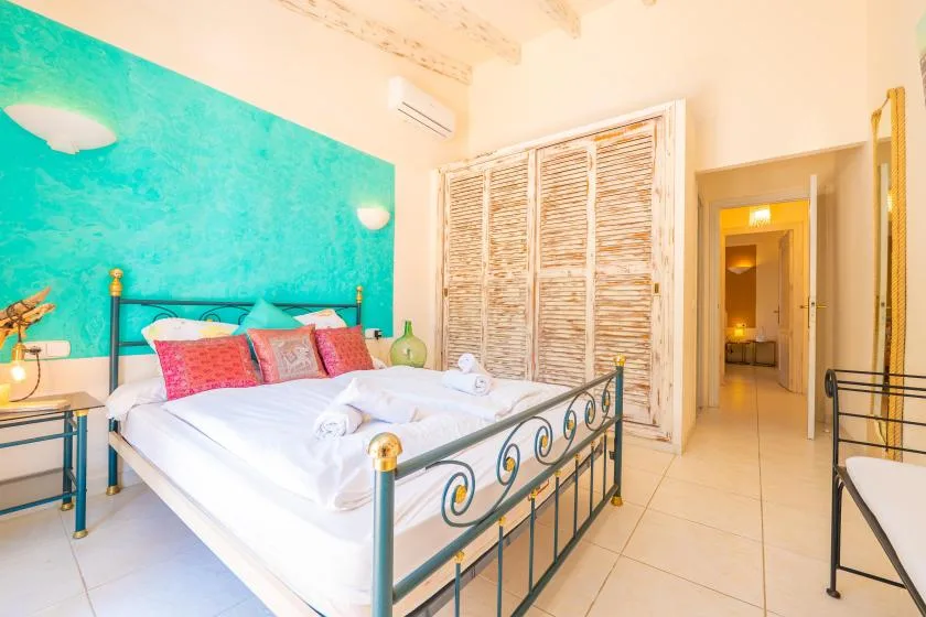 A bedroom with a metal bed, colorful pillows, and a turquoise accent wall.