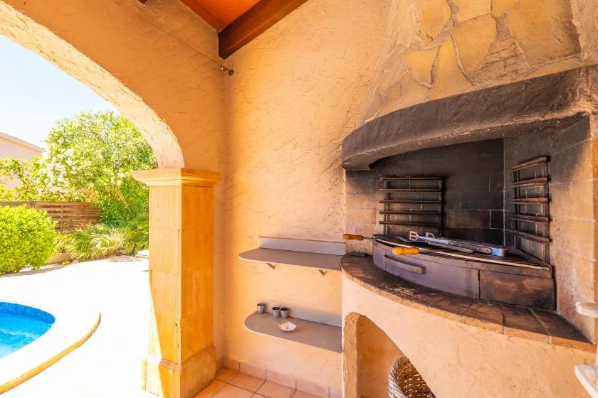 A built-in outdoor grill sits beneath a stone arch beside an open patio.