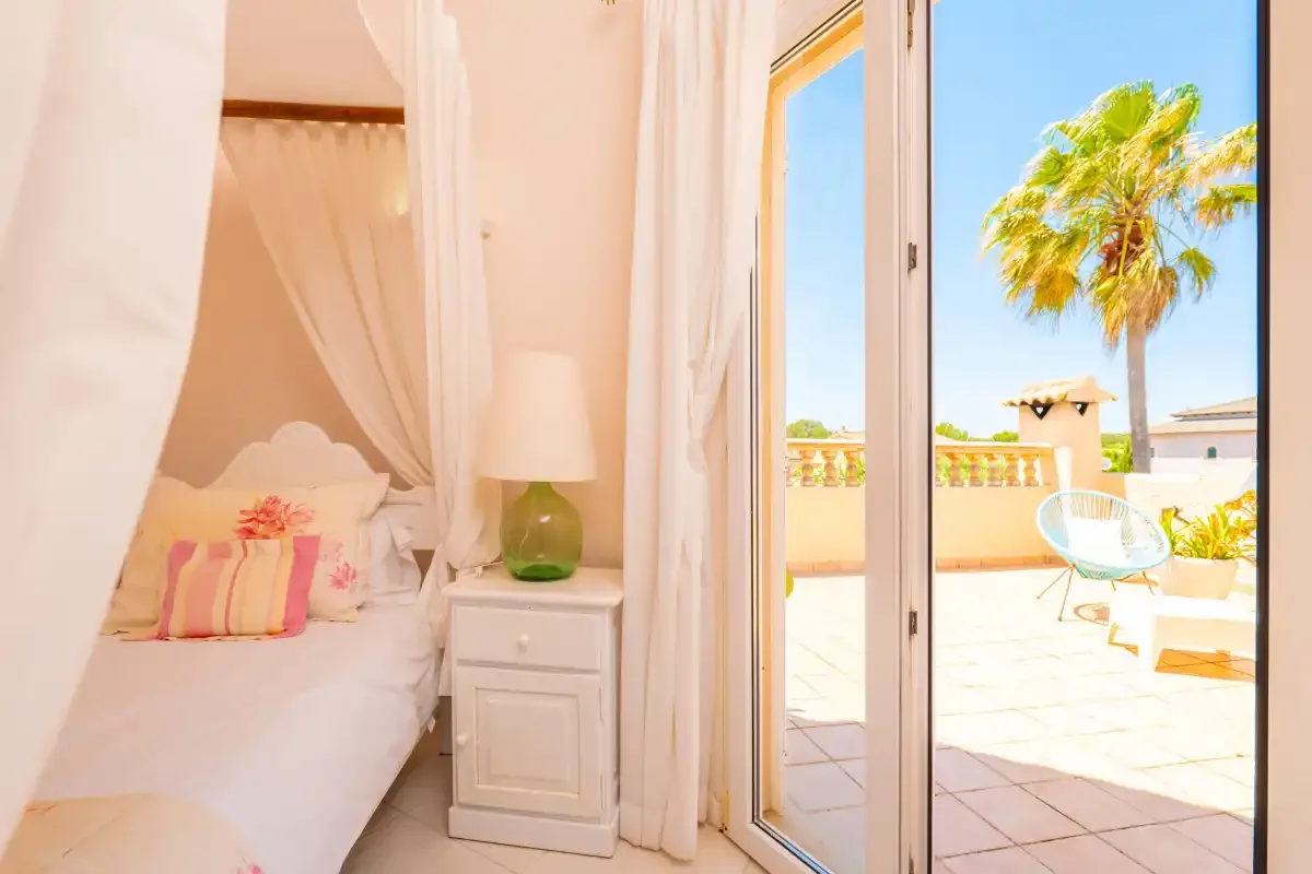 A bright bedroom opens onto a sunlit terrace with outdoor seating.