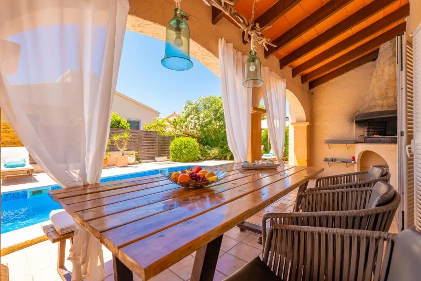 A covered outdoor dining area opens onto a swimming pool and garden.