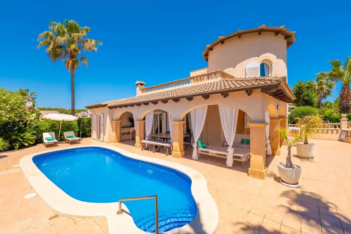 A Mediterranean-style house overlooks a curved swimming pool and sunny patio.