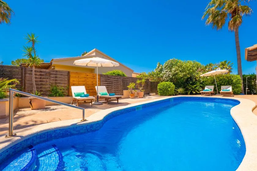 An outdoor swimming pool is surrounded by lounge seating, umbrellas, and greenery.