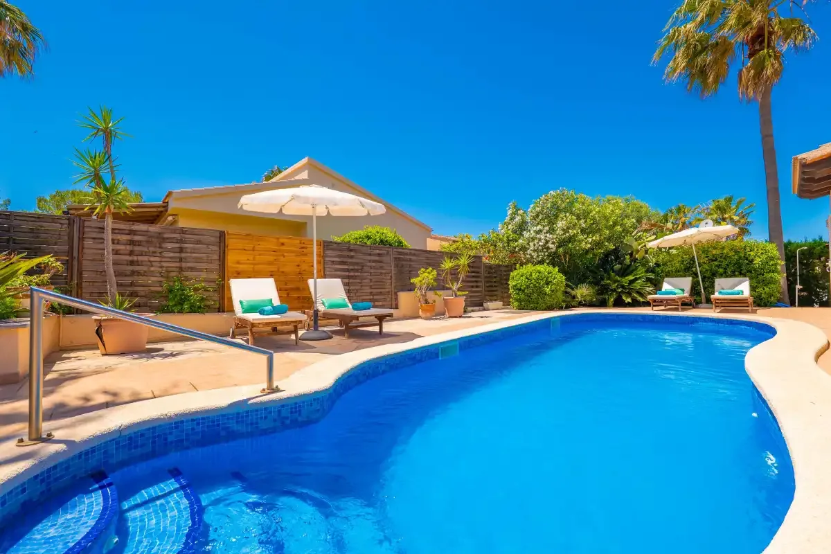 An outdoor swimming pool is surrounded by a deck, lounge seating, and greenery.