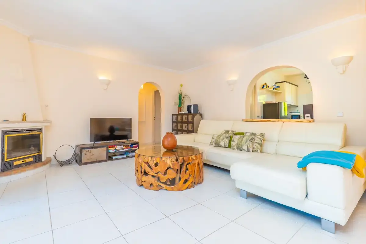 A bright living room with white seating, a television, and a round wooden coffee table.