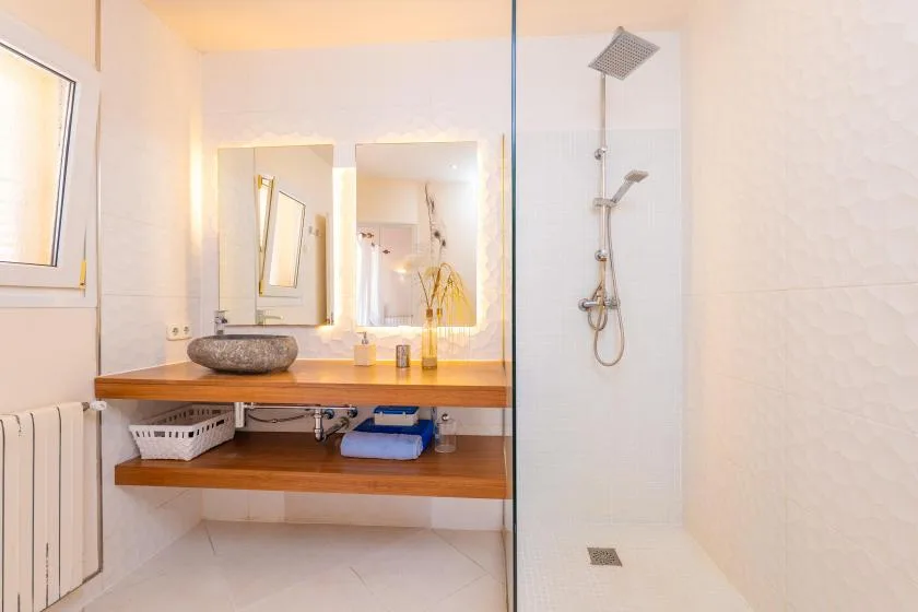 A bright bathroom with a wooden vanity and an open shower area.