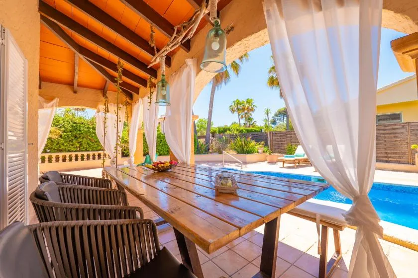 A covered outdoor dining area overlooks a swimming pool and tropical garden.