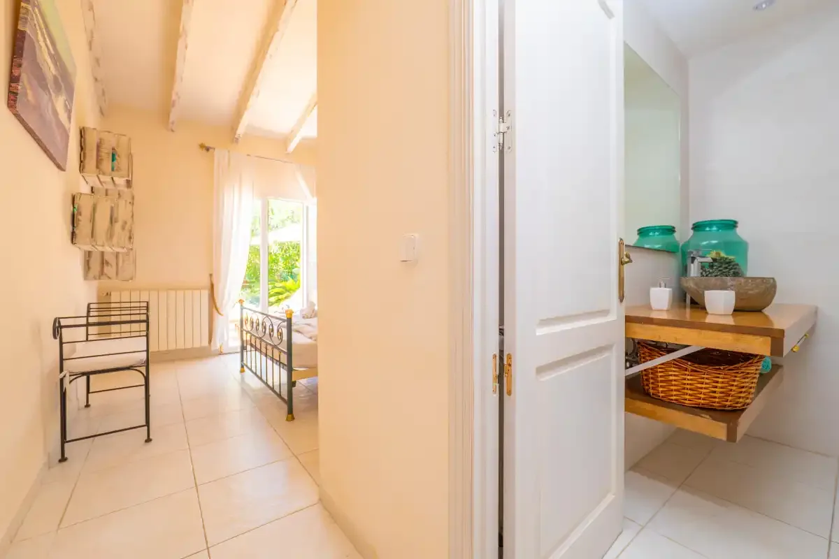 A bright bedroom with two beds and an open door to a small wash area.