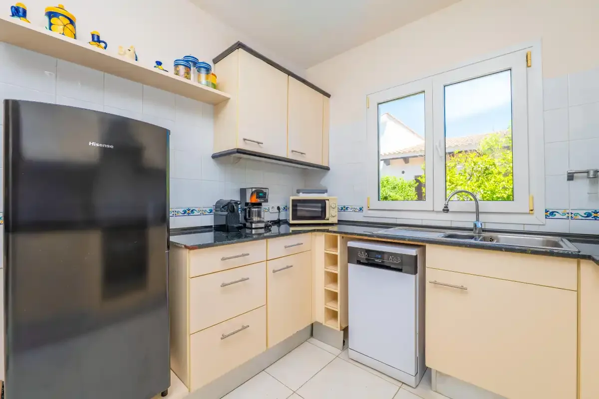 A bright kitchen with light cabinetry, a refrigerator, and a window over the sink.