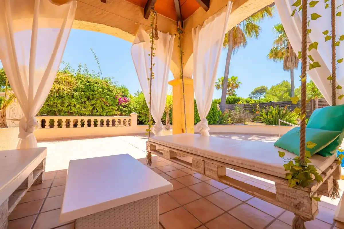 A covered patio with a low table, seating, and views of a sunny garden.