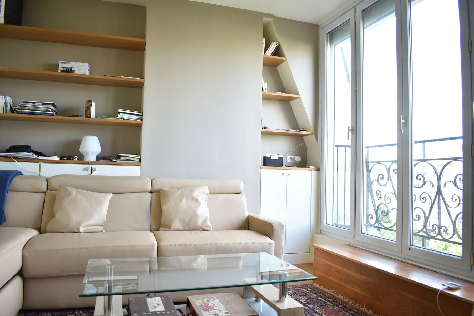 A bright living room with beige seating, built-in shelves, and tall windows.