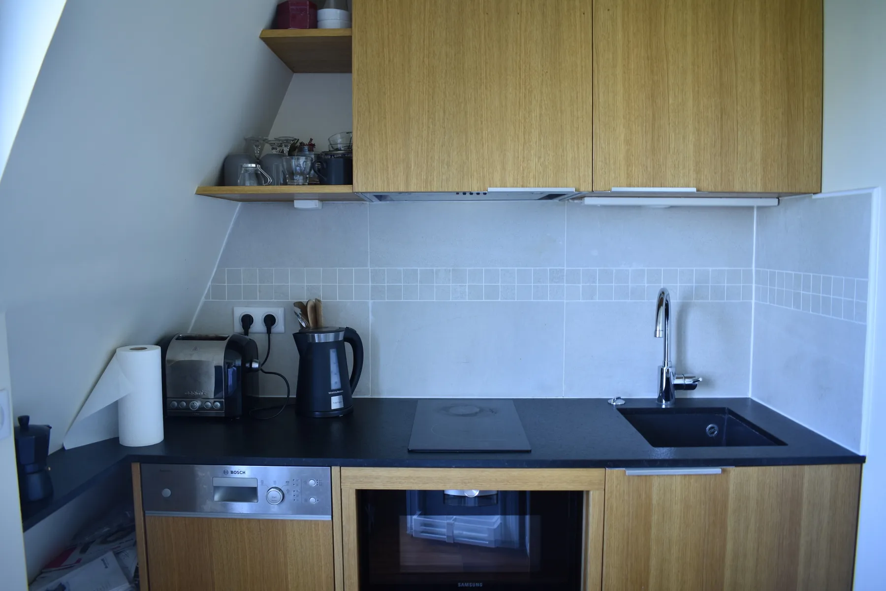 A compact kitchen with wooden cabinets, a dark countertop, and small appliances.