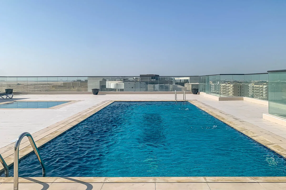 Una piscina en la azotea está junto a una terraza pavimentada y una barandilla de vidrio.
