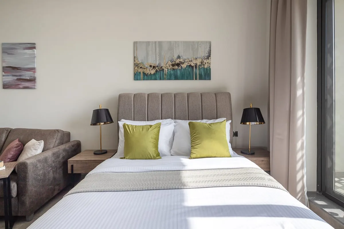 Un dormitorio con una cama bien tendida y cojines decorativos verdes.