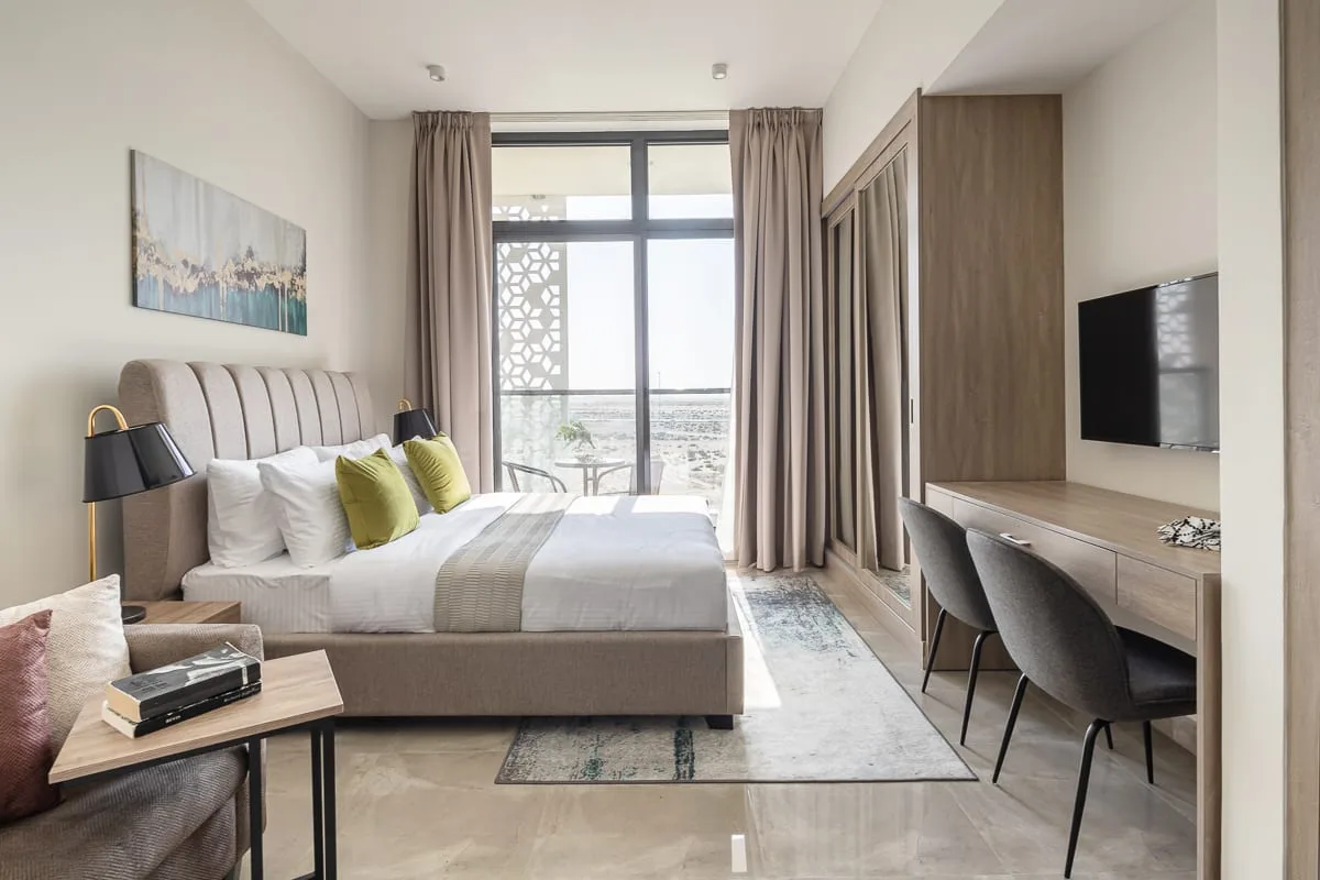 Dormitorio con una cama junto a grandes ventanales y un escritorio.