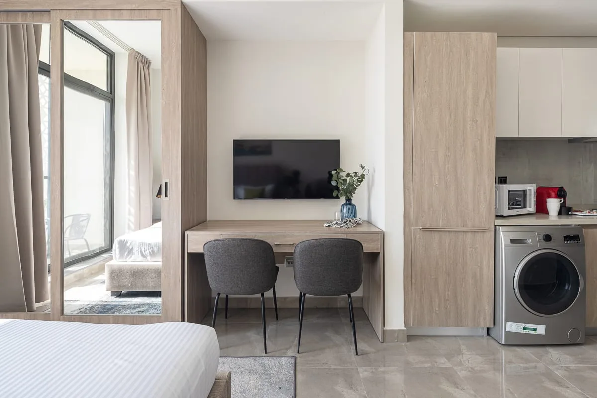 Un dormitorio con escritorio y televisor junto a una pequeña zona de cocina.