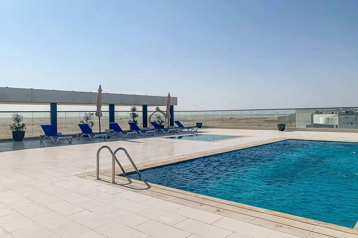 Una piscina en la azotea junto a una terraza de baldosas con asientos y sombrillas cerradas.