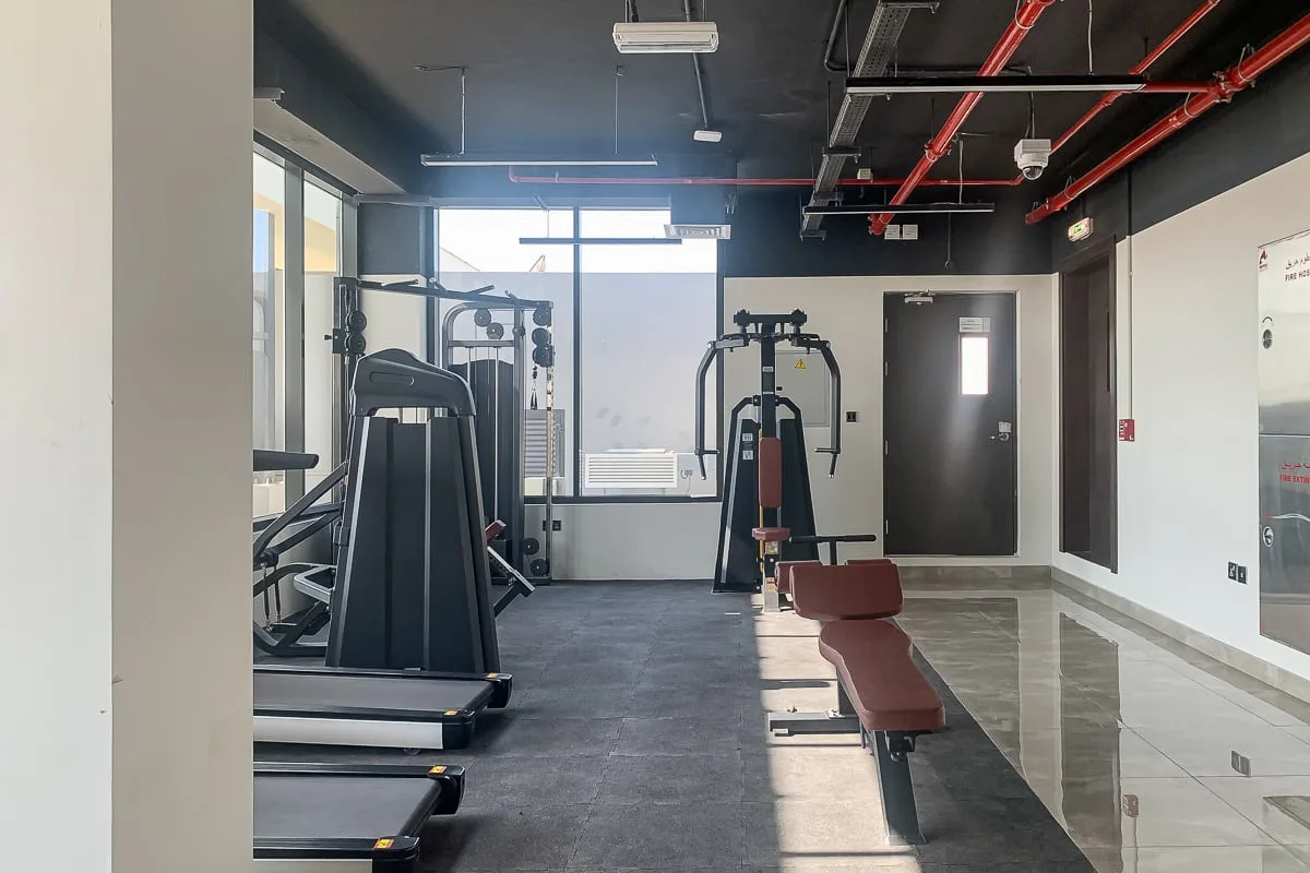 Un gimnasio con máquinas de ejercicio y un banco de pesas junto a un pasillo de baldosas.
