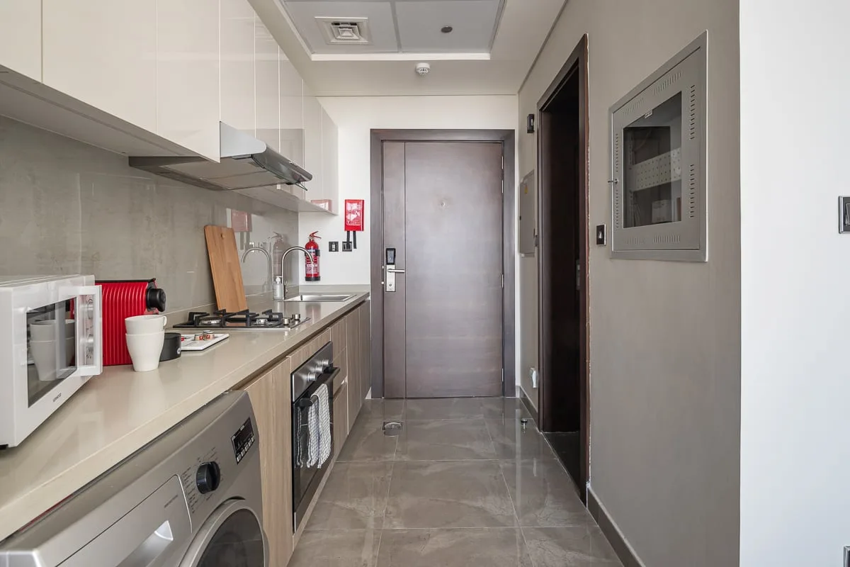 Una cocina estrecha con lavadora y encimera de cocción conduce a una puerta cerrada.