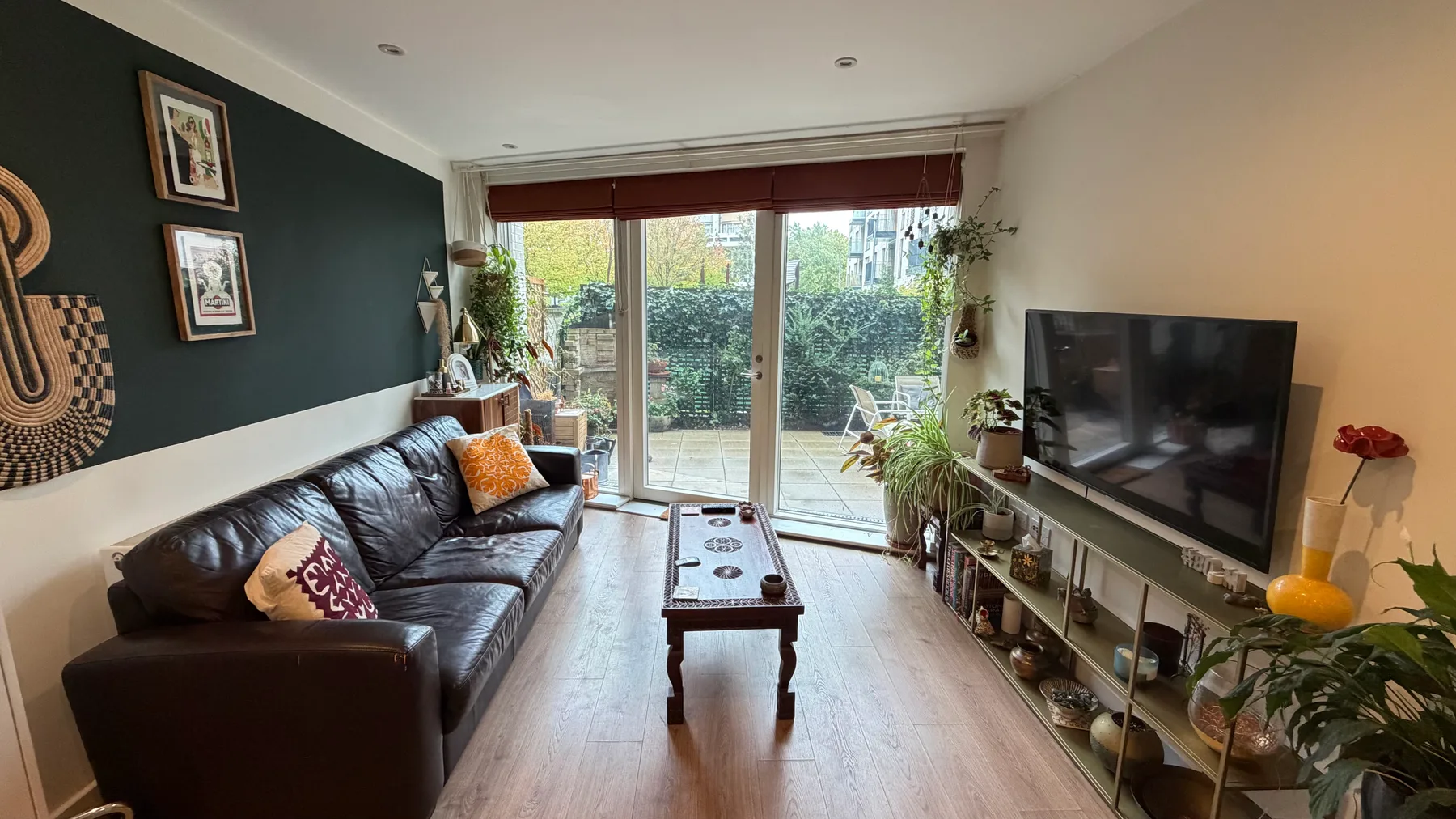 Sala de estar con asientos, un televisor y puertas de vidrio que dan al jardín.