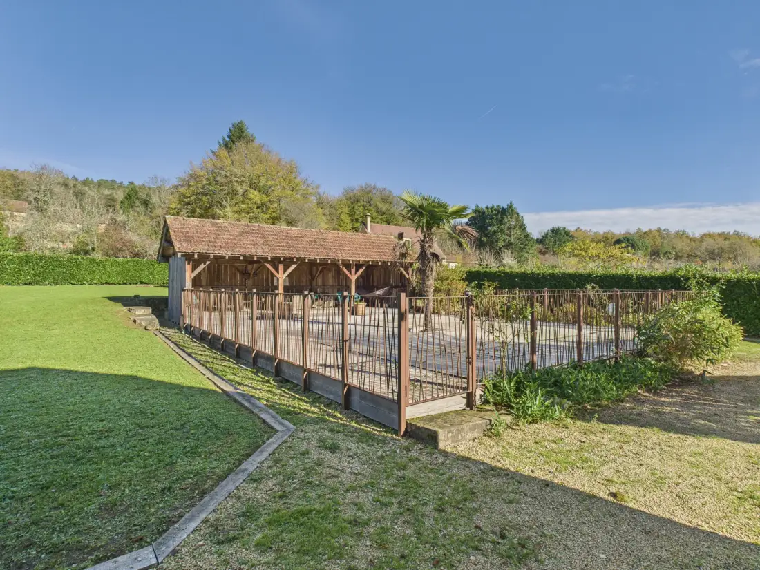 An outdoor swimming pool is enclosed by a fence beside a wooden shelter.