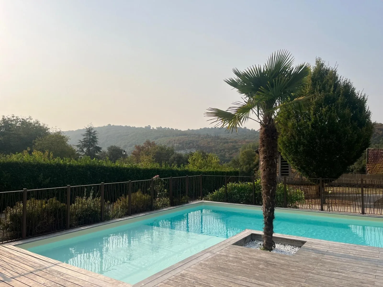 Una piscina al aire libre está rodeada por una terraza de madera y vegetación.