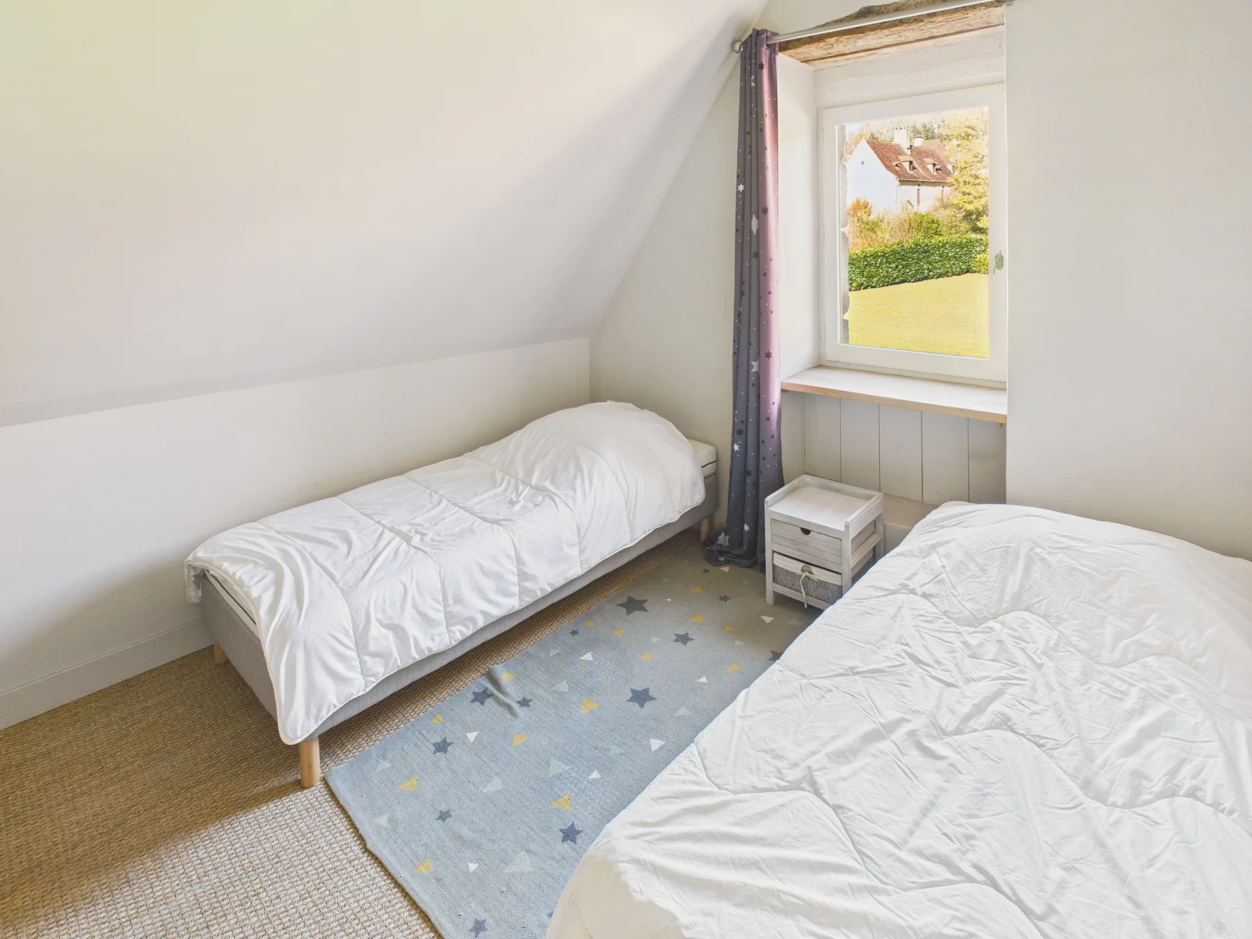 A bright bedroom with two beds, a patterned rug, and a window.