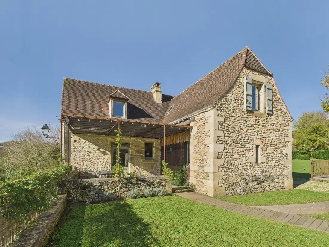 A stone house stands beside a grassy garden under a clear sky.