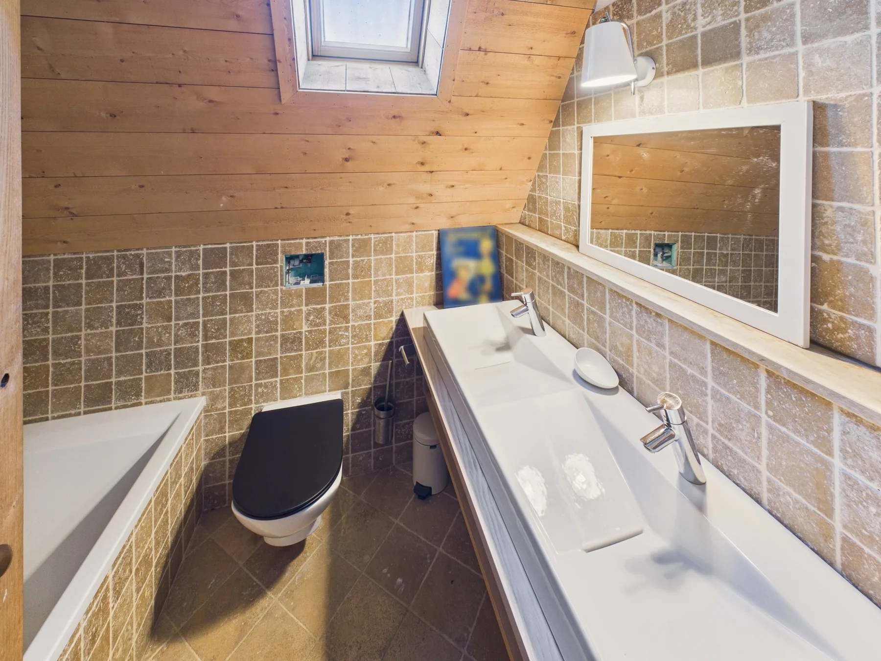 A tiled bathroom with a bathtub, toilet, and sink beneath a sloped wooden ceiling.
