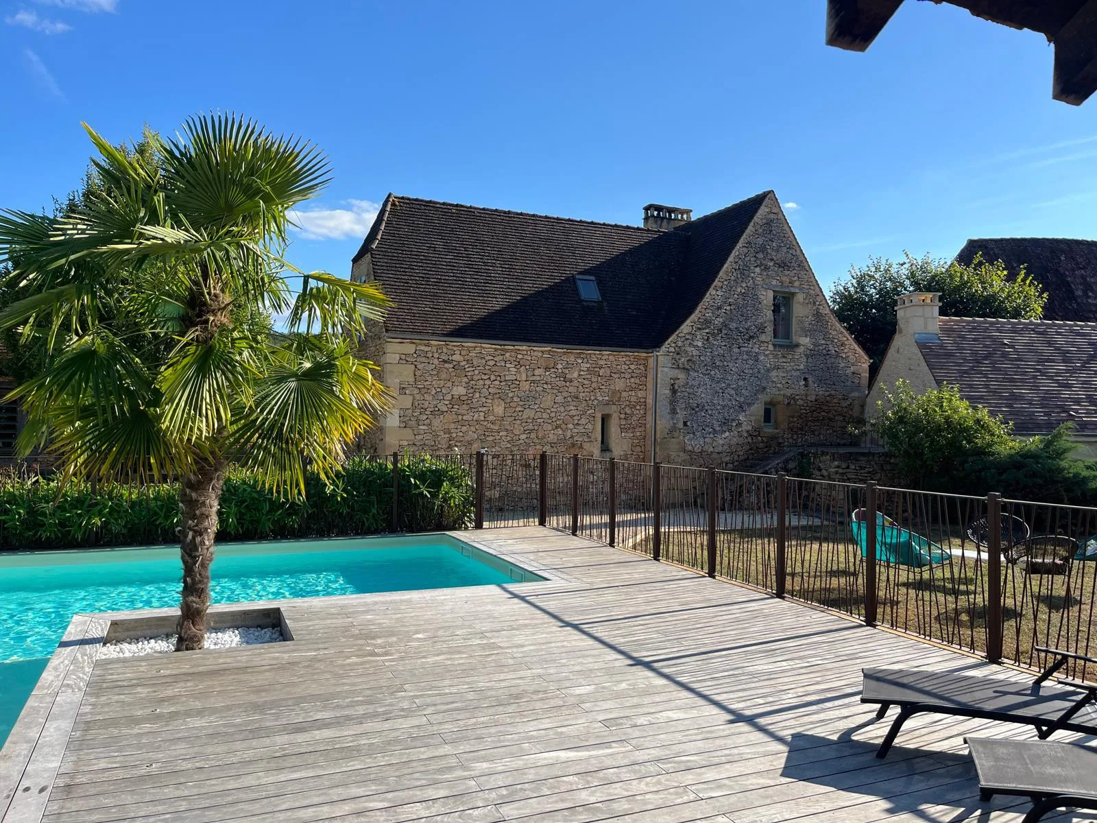 A swimming pool and wooden deck sit in front of a stone house.