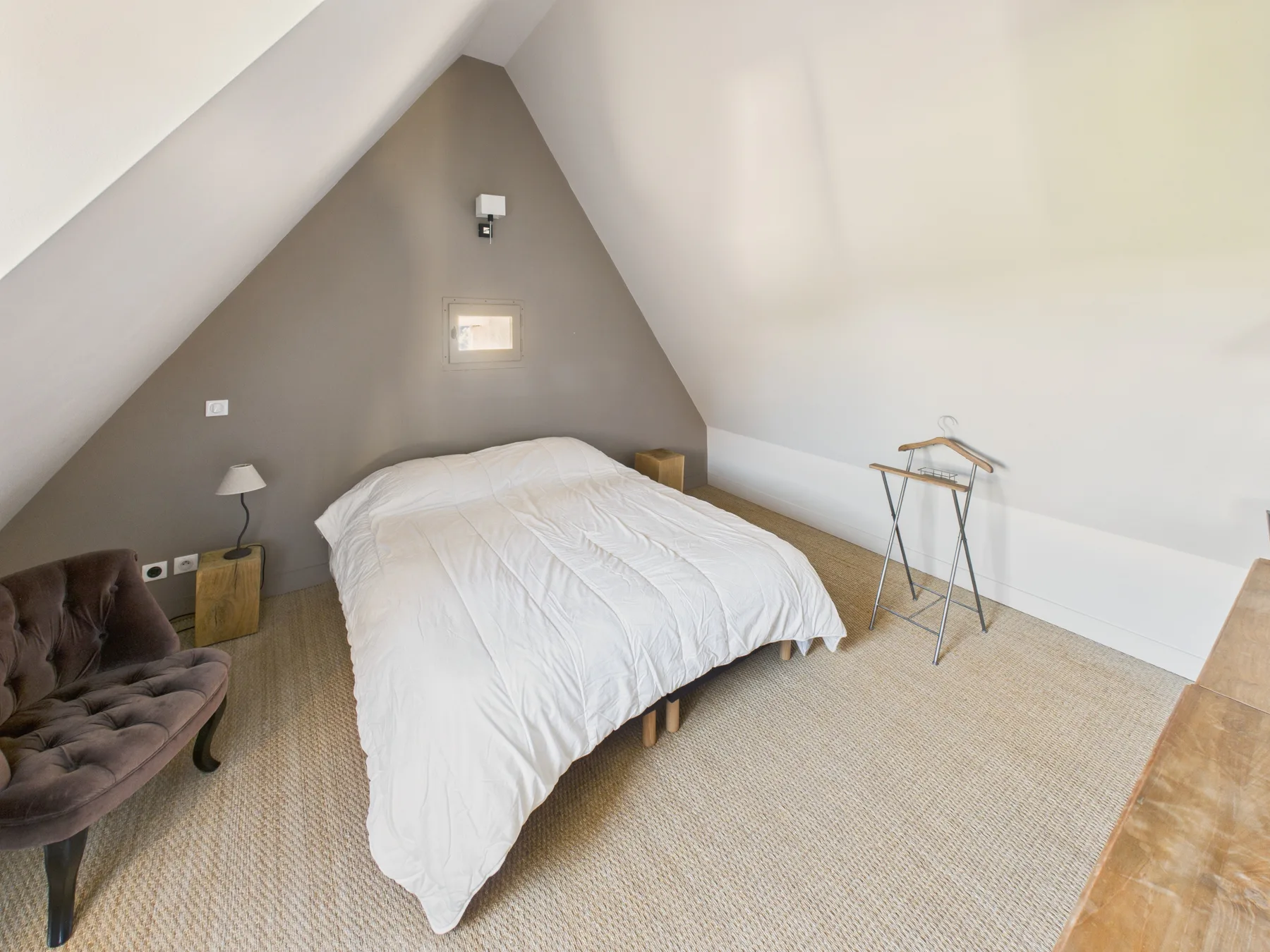 A bedroom with a bed beneath a sloped ceiling and a small seating area.
