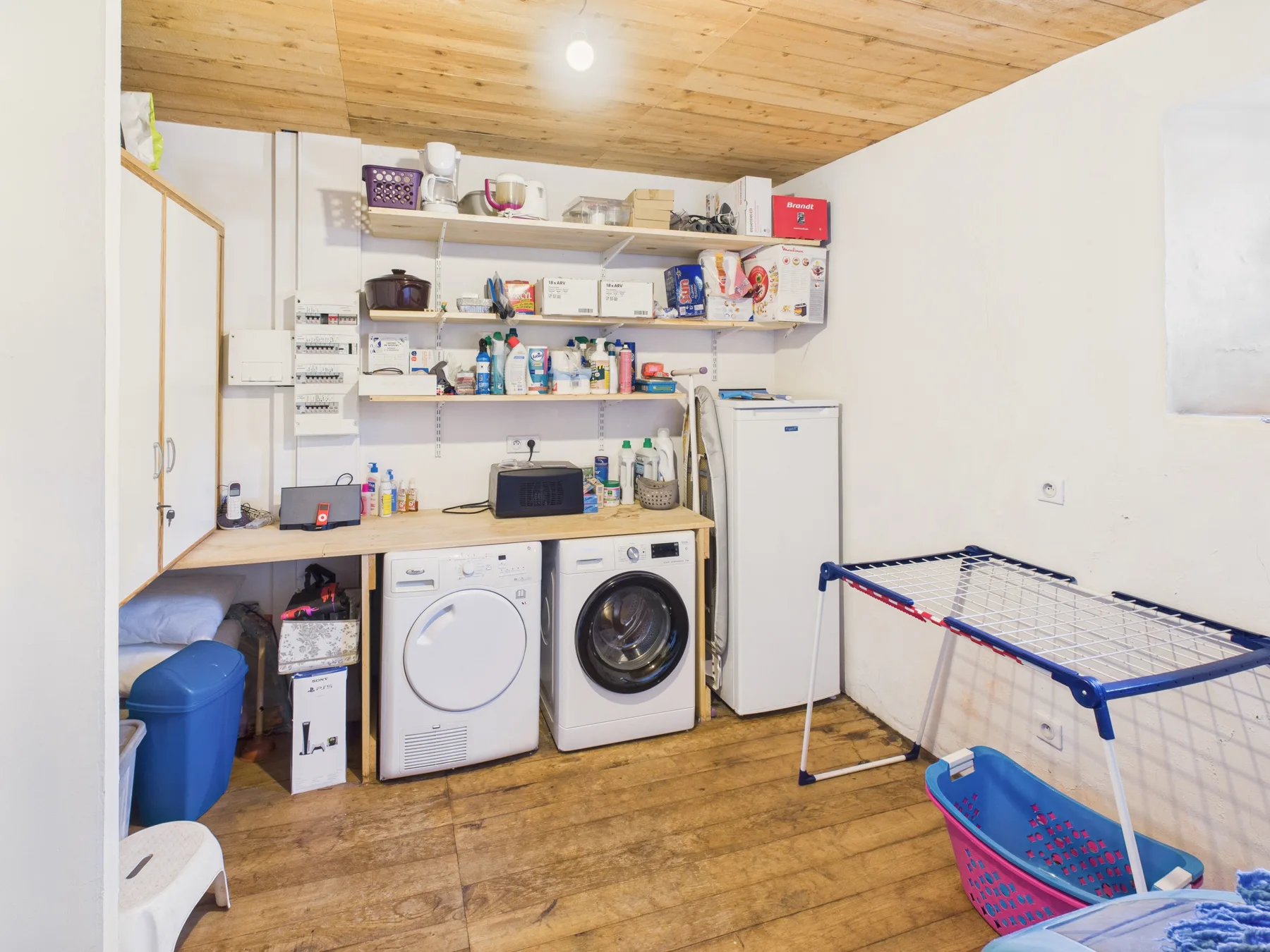 A laundry room with washing machines, storage shelves, and a drying rack.