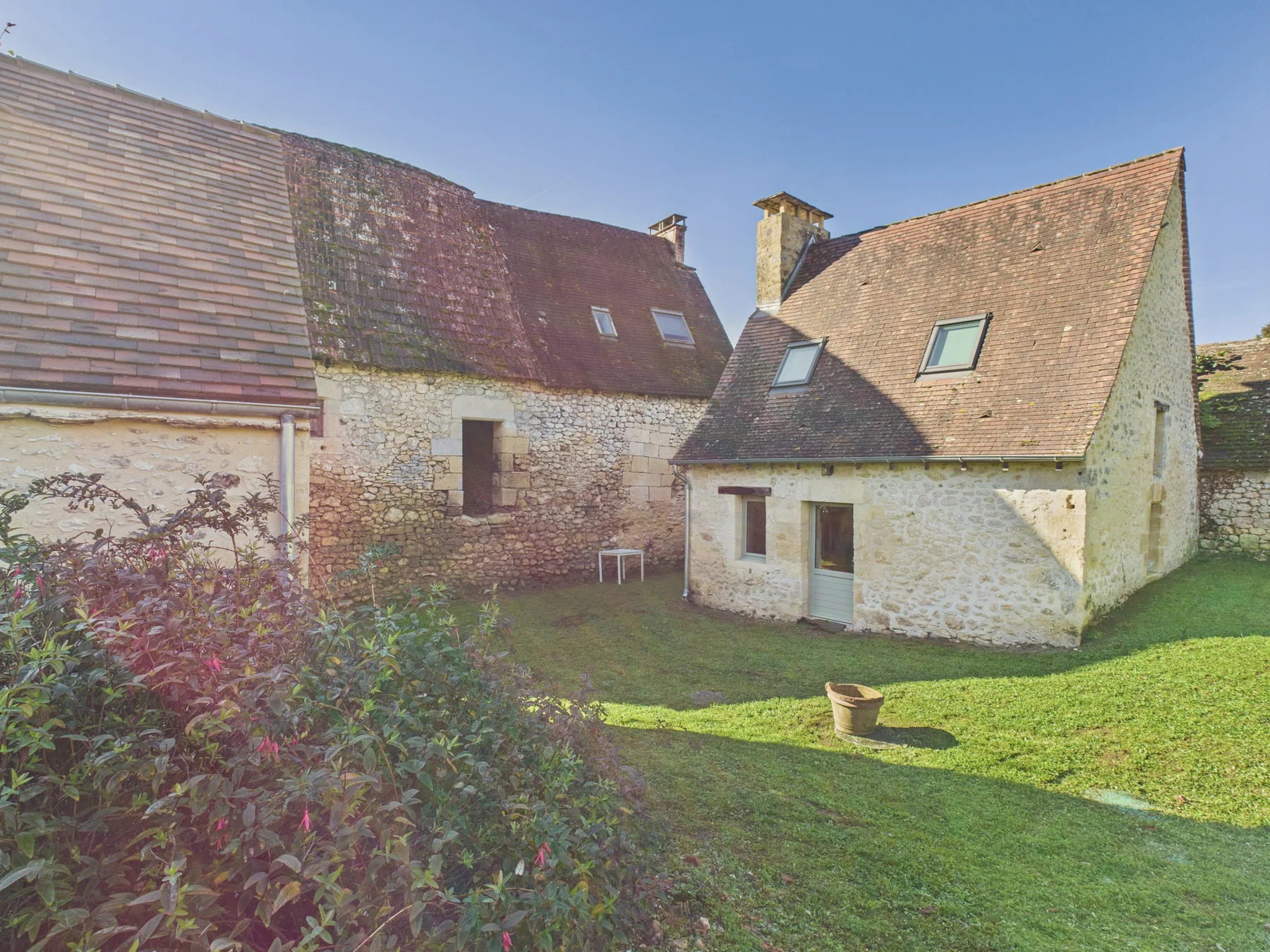 A stone house with steep tiled roofs sits beside a grassy yard.