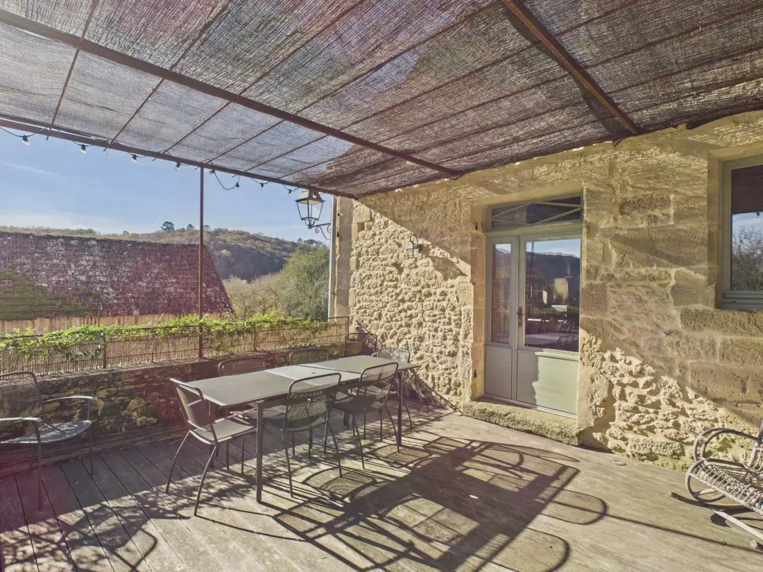 A covered stone patio with an outdoor dining table and chairs.