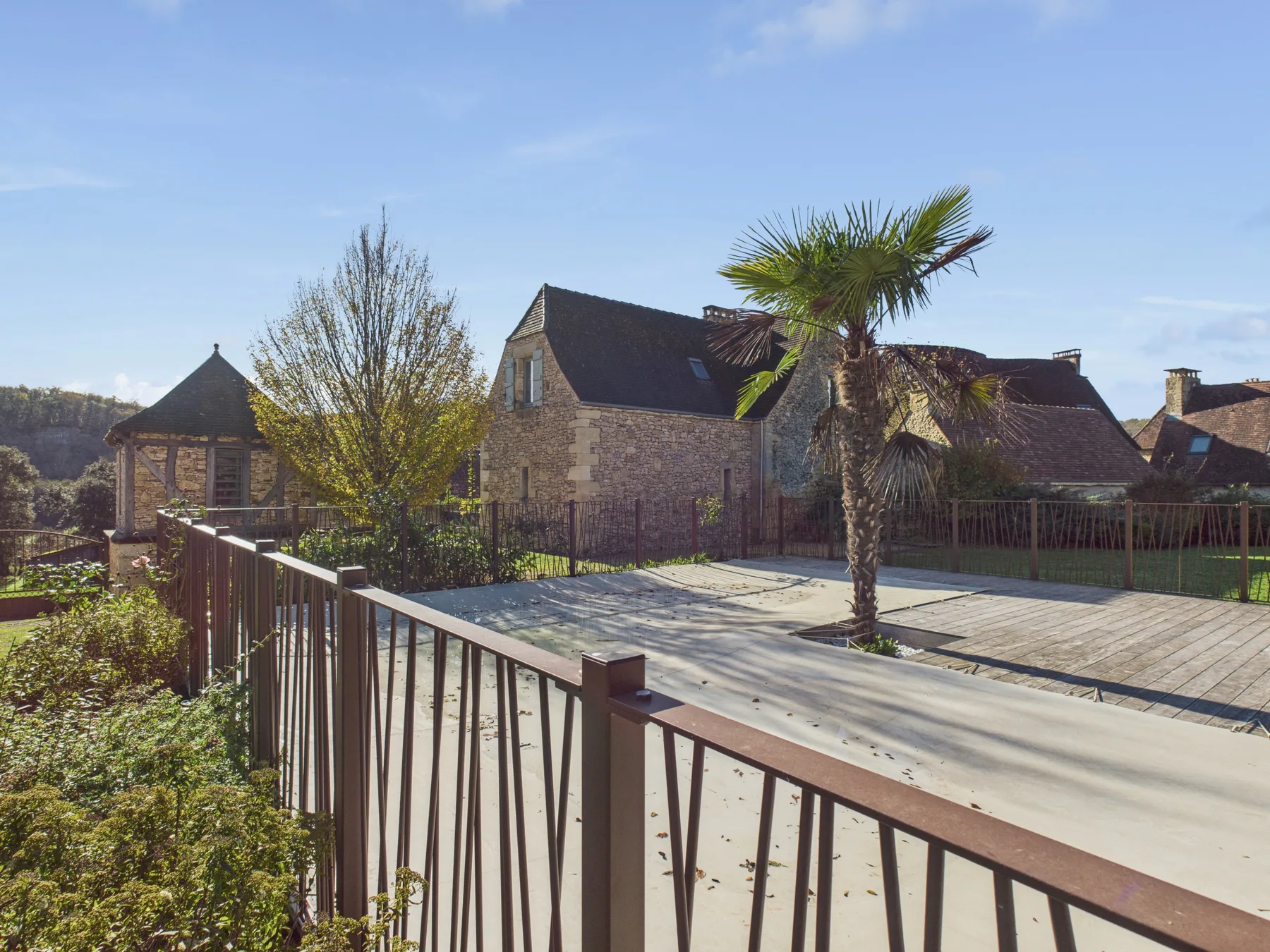 A sunny outdoor terrace overlooks stone buildings and a palm tree.
